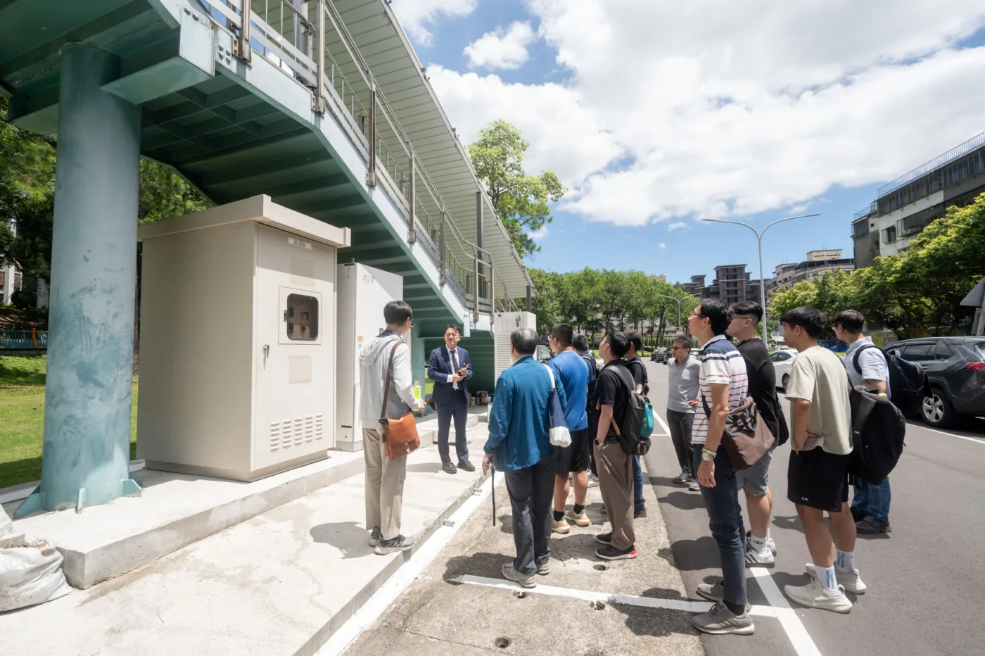 歩道橋の太陽光発電から蓄電・充電設備へ、現地でシステム統合について説明。